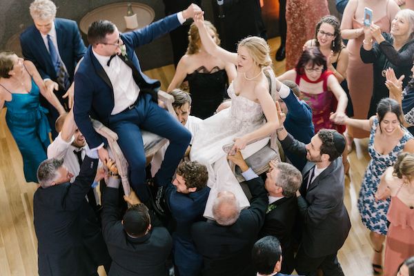 bride and groom being lifted on chairs during their hot