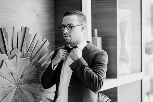 black and white photo of a groom fixing his bow tie before his wedding 