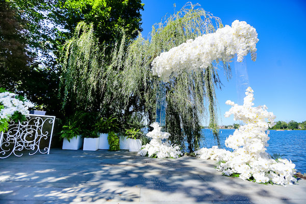 Waterfront wedding ceremony with a clear acrylic wedding structure draped in white Phalaenopsis orchids