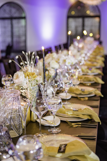 long feating table with eclectic vessels filled with flowers and elegant place setting