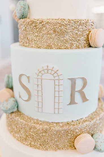 close up of gold and white wedding cake with custom monogram and French macarons 