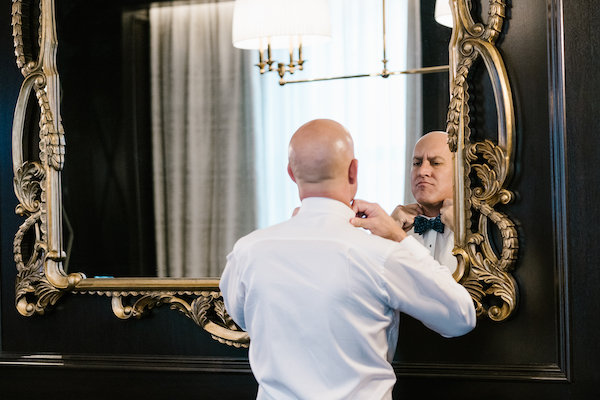 Groom fixing his bow tie before his wedding