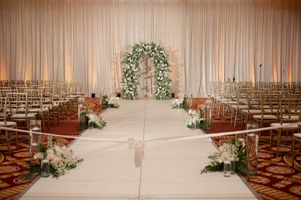 White aisle dotted with flowers and candles leading to a lush floral arch