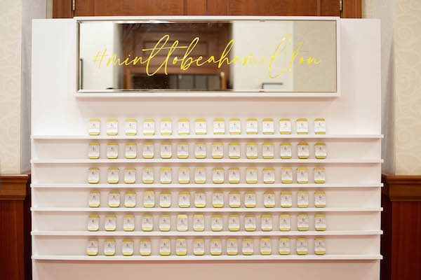 Custom escort card wall with tins of mints and the couple's wedding hashtag on the top