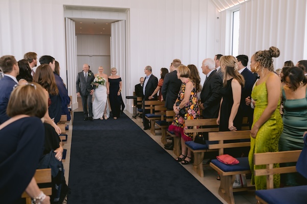 A bride and her parents walking down the aisle of the Straits Chapel at her wisconsin destination wedding.