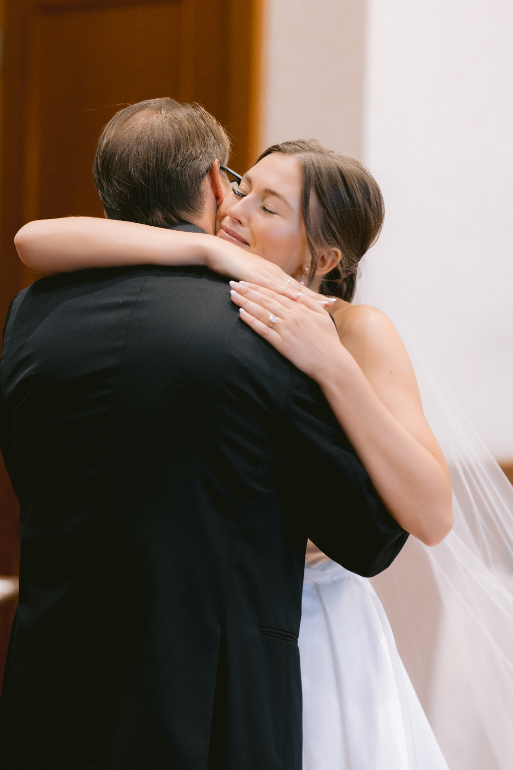 The bride embraces her father in a heartfelt hug, eyes closed, as they share a special first look moment before the ceremony.