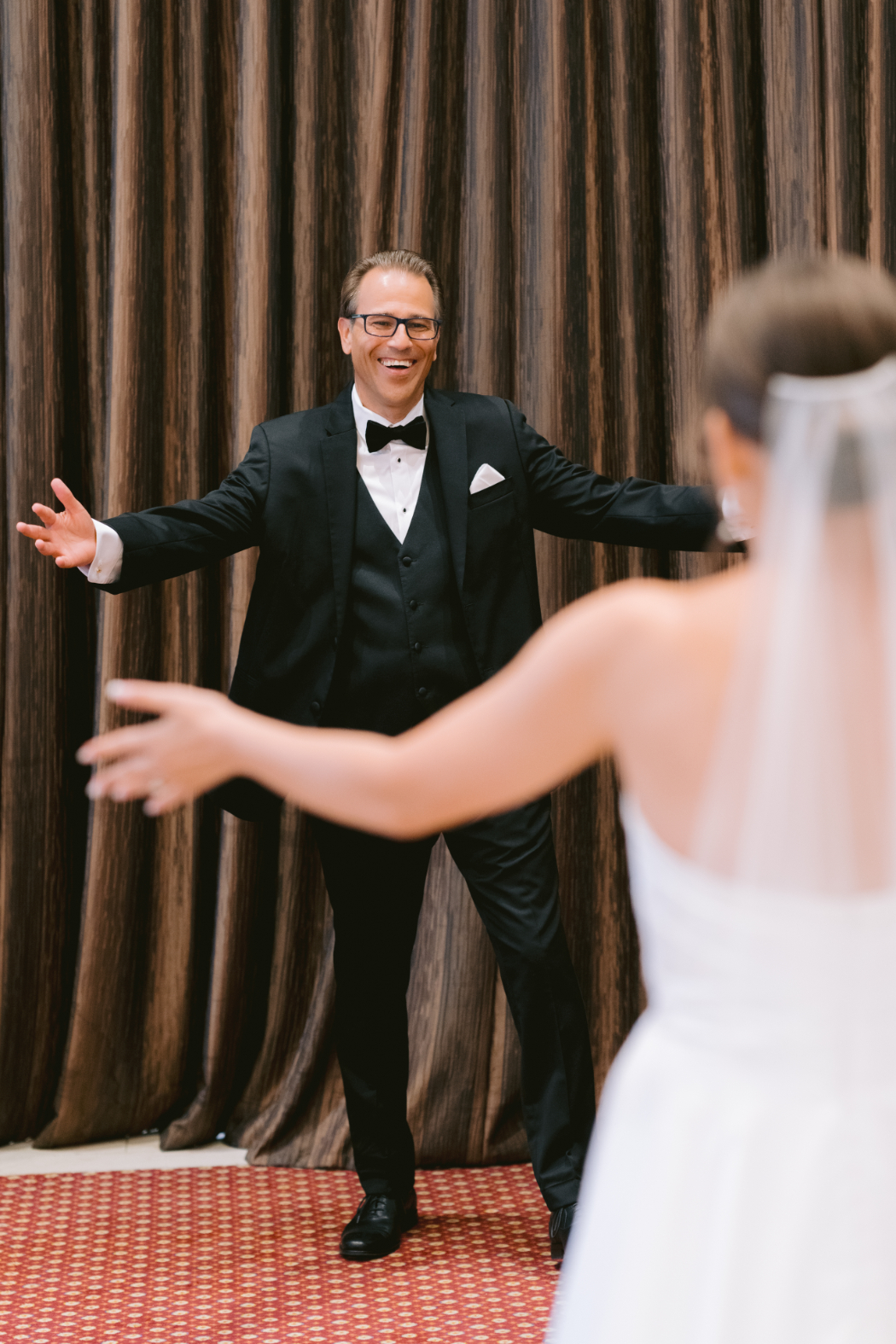 The bride’s father stands with open arms, ready to embrace his daughter during their emotional first look.