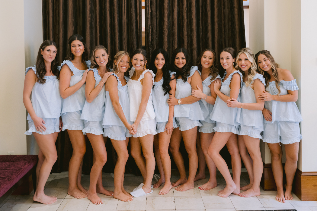 A bride and her bridesmaids in matching light blue pajama sets pose together.