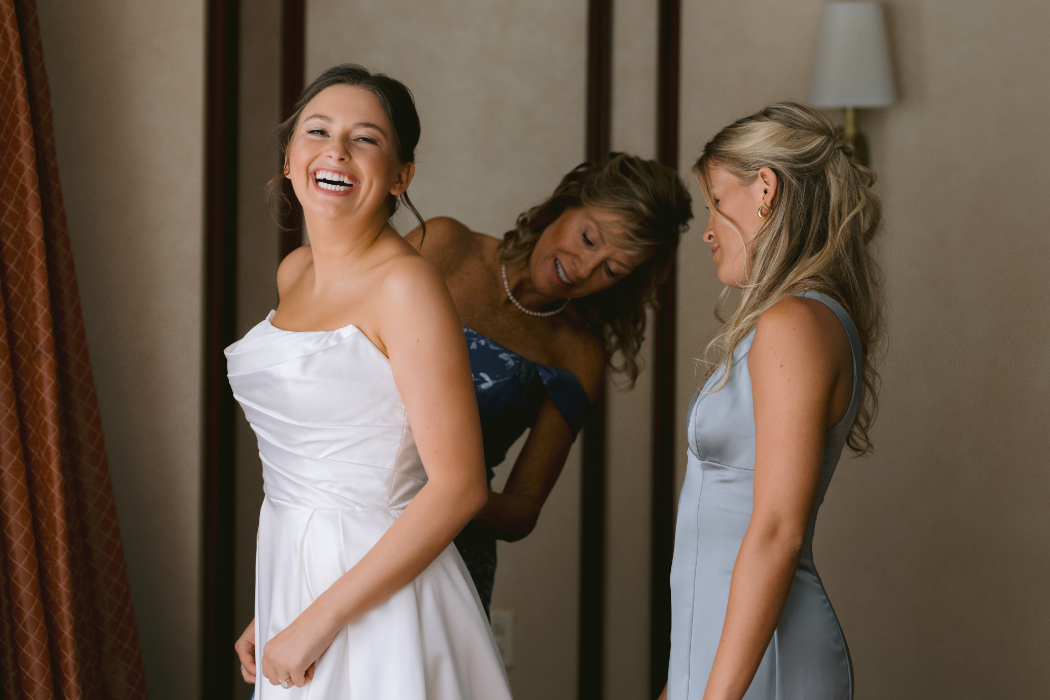 A bride, assisted by her mother and bridesmaid, gets into her gown.