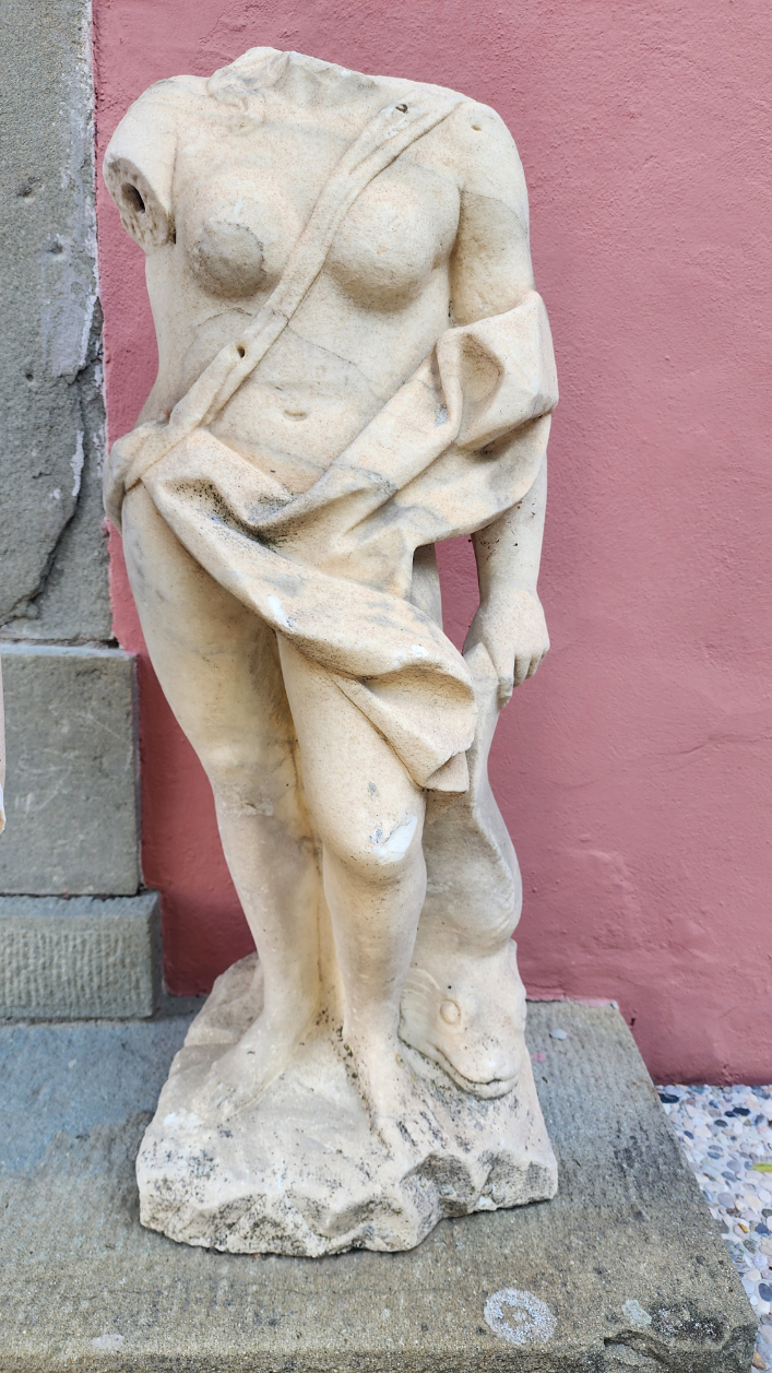 A weathered Italian marble bust of a classical figure, set against a muted pink wall.