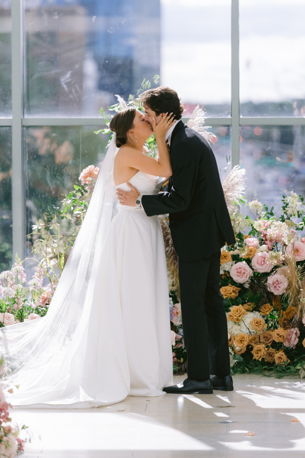 Bride and groom share their first kiss at the altar, framed by lush floral arrangements.